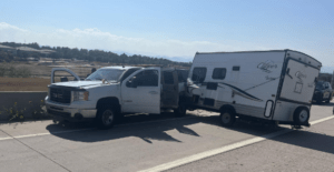 Photo of jackknifed white truck towing a camper trailer.